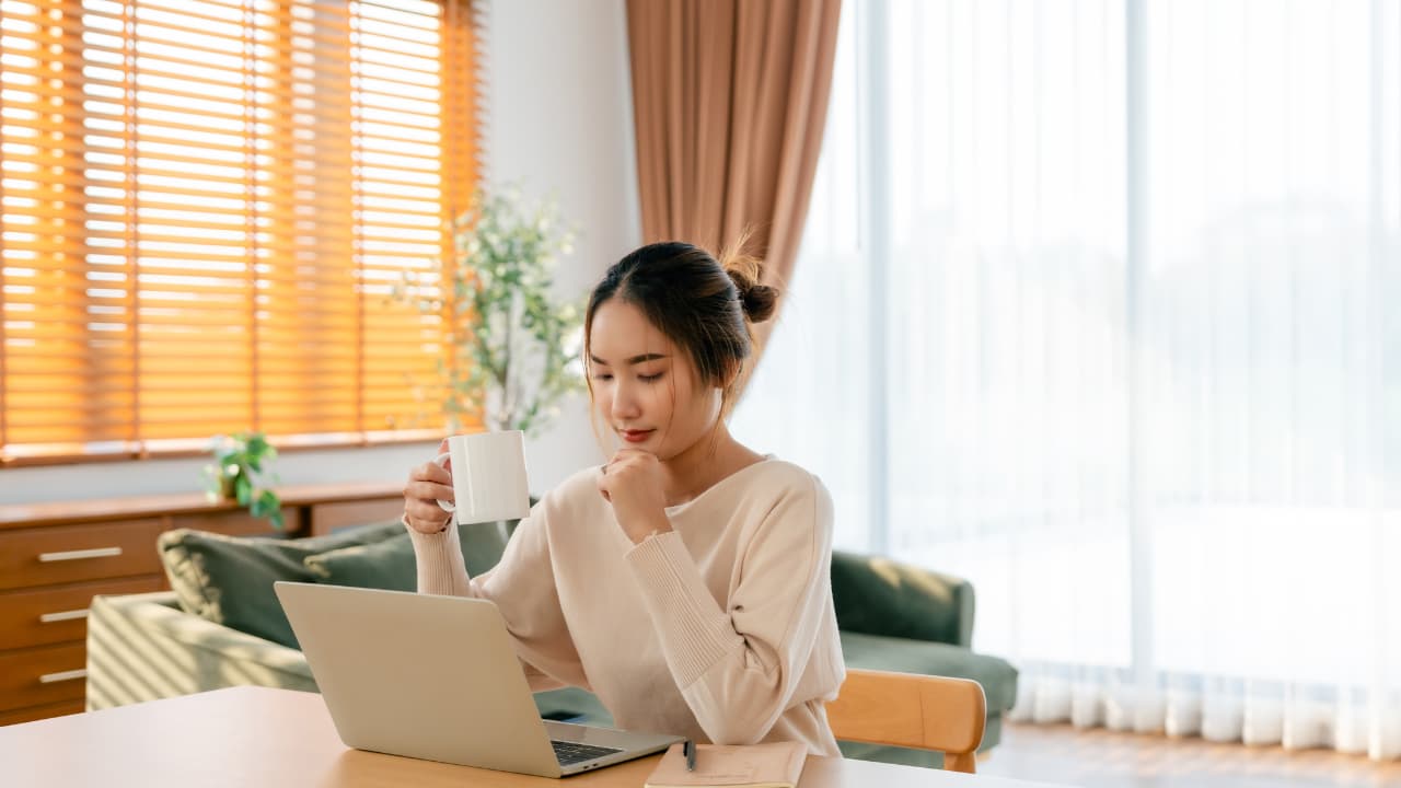 コーヒーを持ちながらPCを見る女性